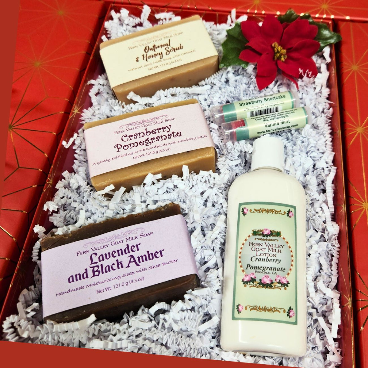 An open premium holiday gift box filled with clean white crinkle paper, three labeled Fern Valley goat milk soaps (Oatmeal & Honey, Lavender Black Amber, Cranberry Pomegranate), a bottle of lotion, and two lip balms.