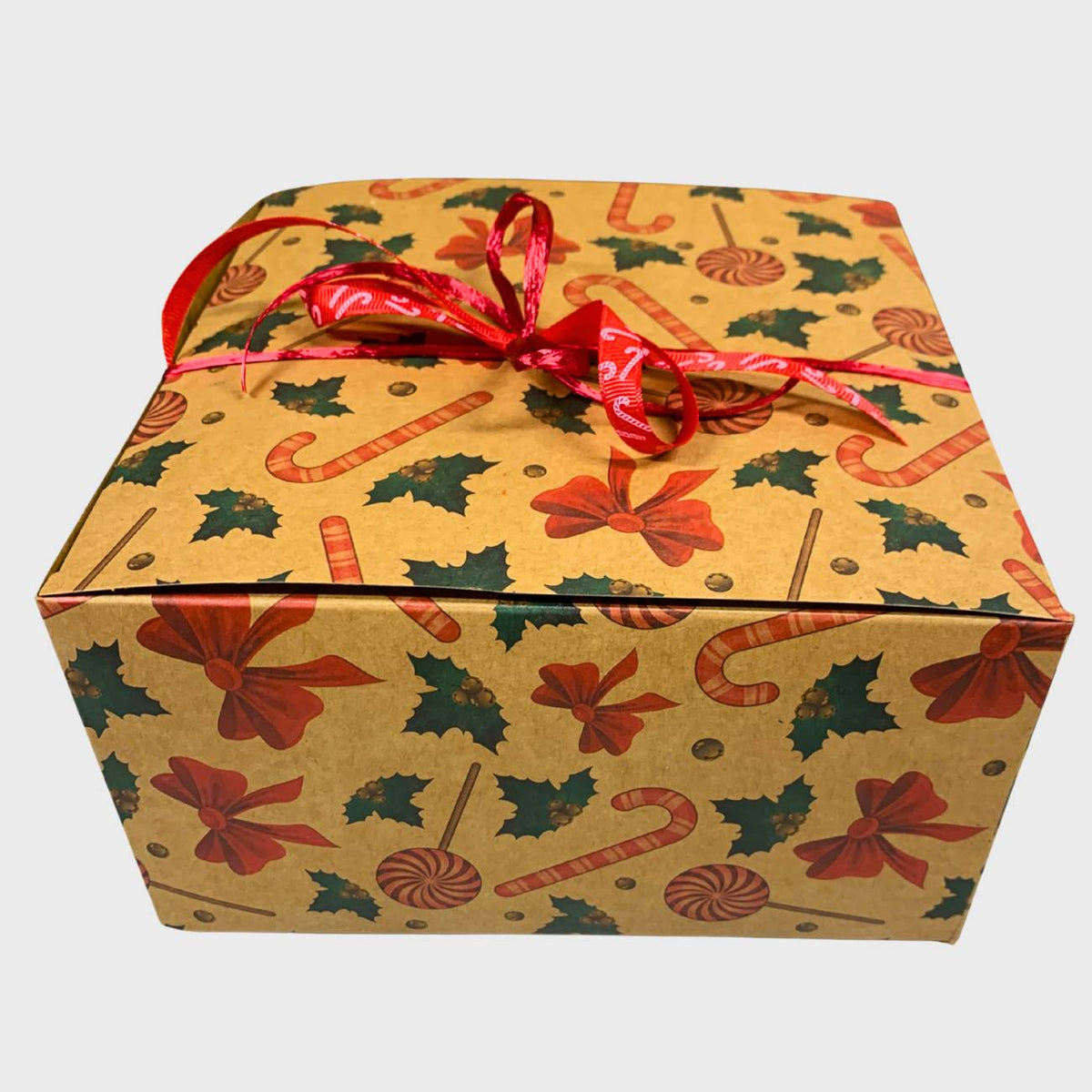 Gift box with Christmas-themed pattern of candy canes, bow, and holly with a red ribbon on a white background