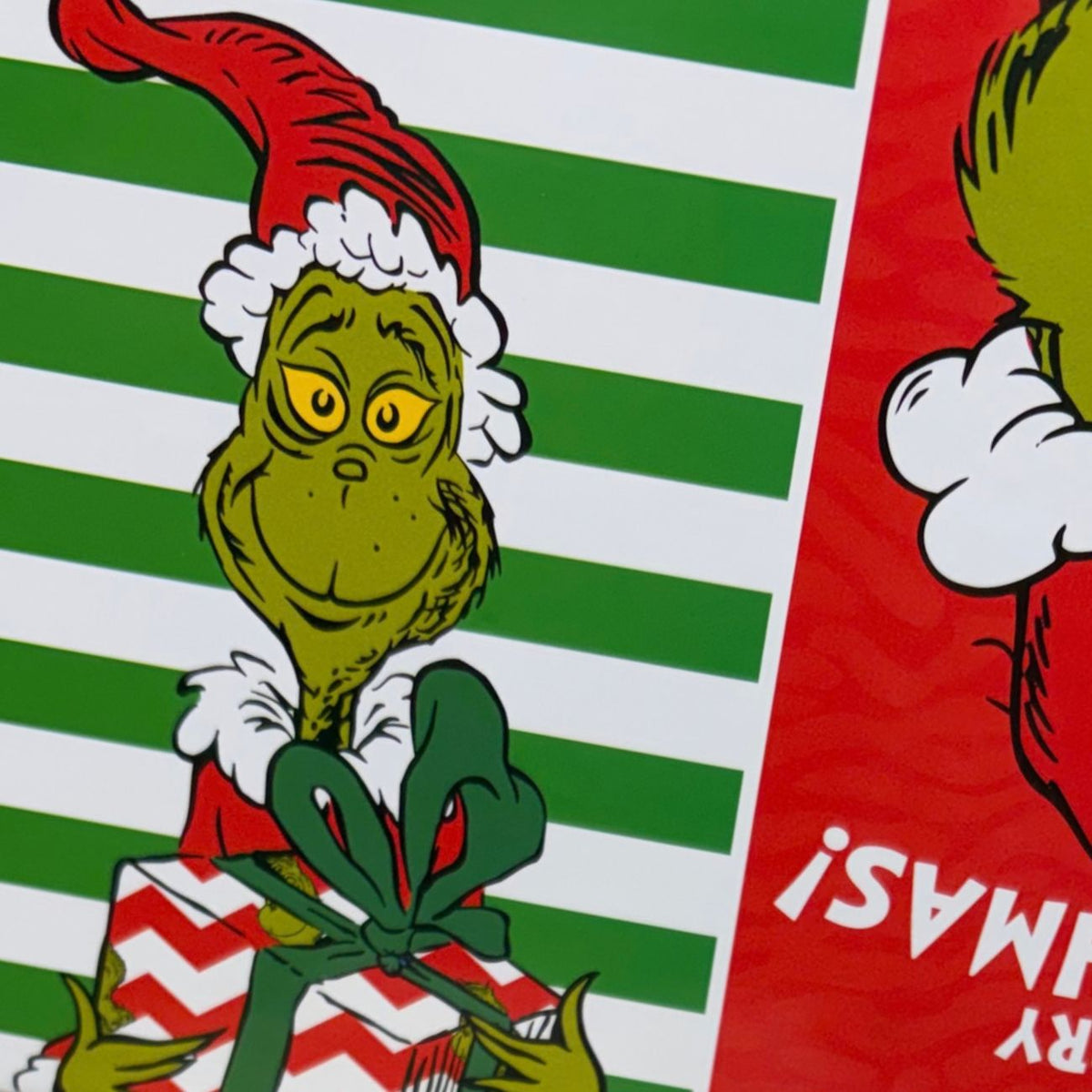 A close-up graphic view of the festive red and green striped Christmas gift box pattern featuring an illustration of the classic animated Grinch character holding a wrapped holiday present with a big green bow.