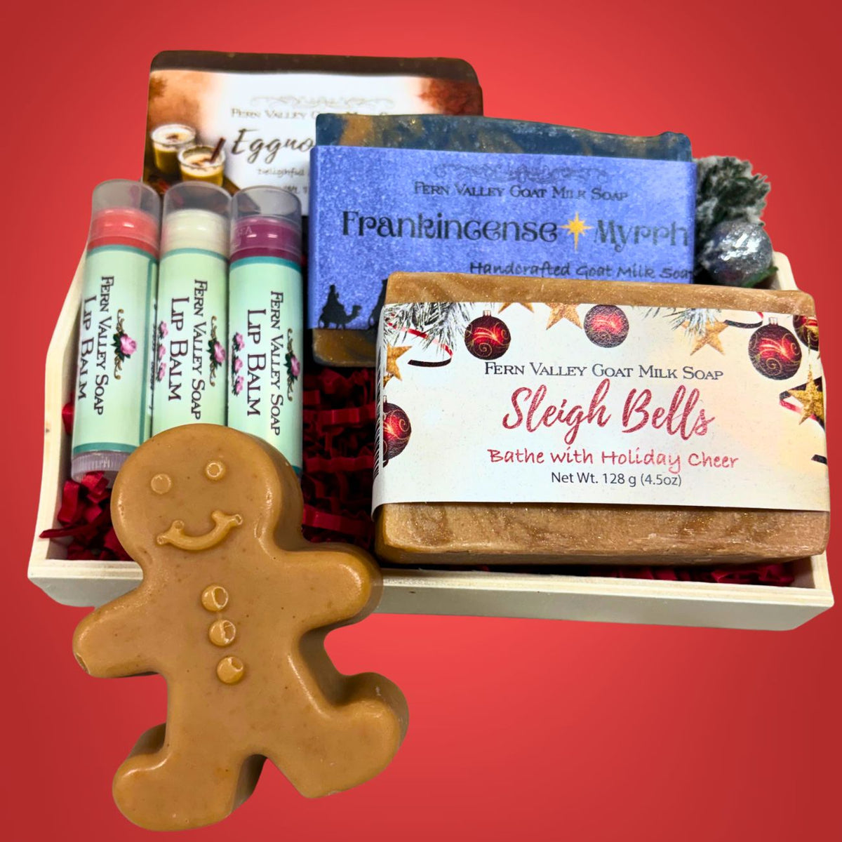 A gift basket filled with Fernd Valley Goat Milk Soap products and lip balms, including a gingerbread-shaped soap bar in the foreground, a blue Frankincense + Myrrh soap bar, and a &