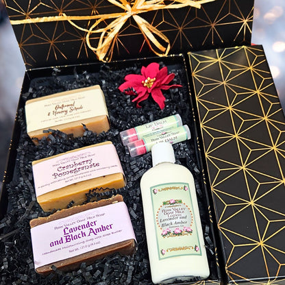 An open premium holiday gift box filled with clean white crinkle paper, three labeled Fern Valley goat milk soaps (Oatmeal &amp; Honey, Lavender Black Amber, Cranberry Pomegranate), a bottle of lotion, and two lip balms.