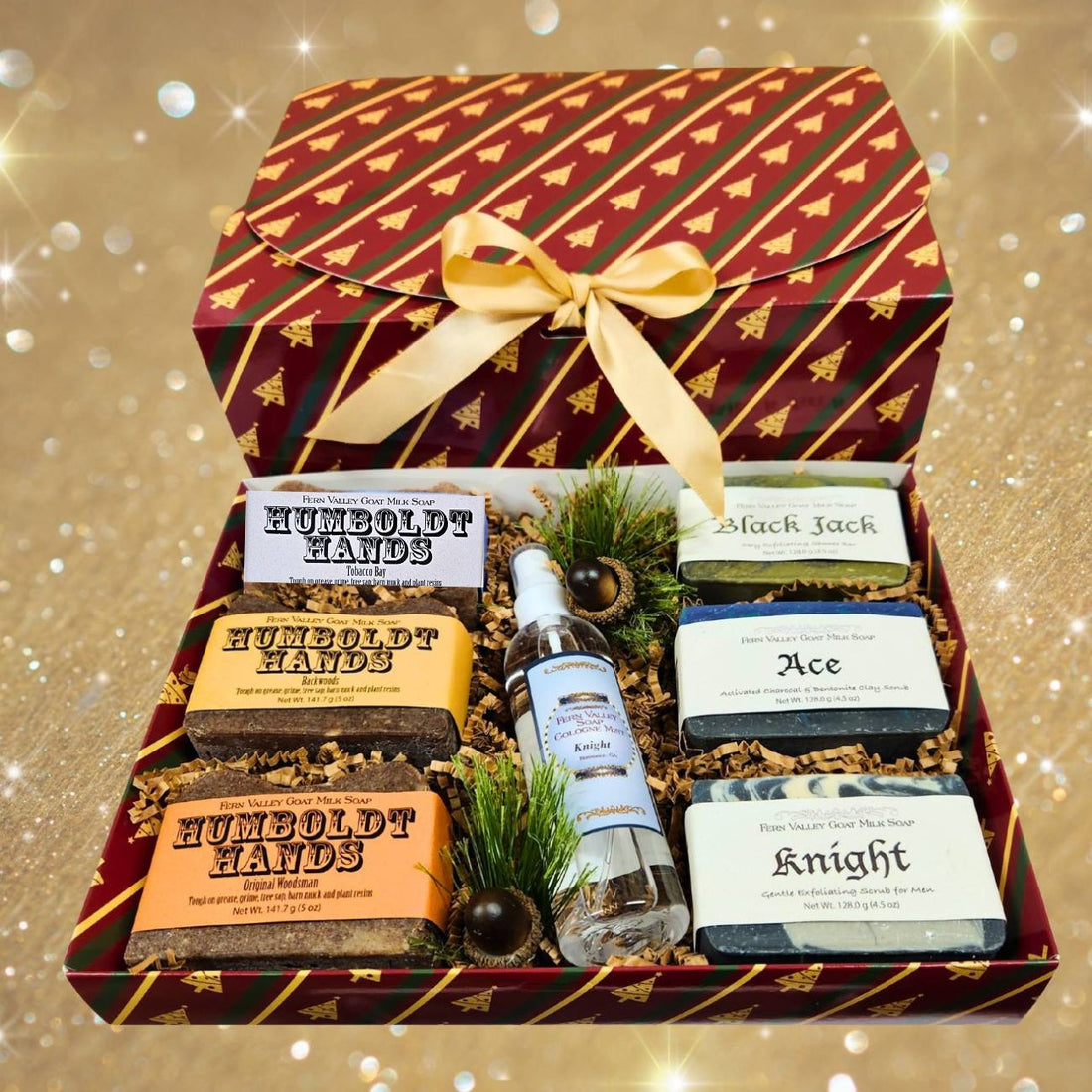 A Christmas-themed gift set in a red patterned box with a gold bow, containing handcrafted soaps and a bottle of cologne, arranged in a decorative box with pine branches and acorns. 