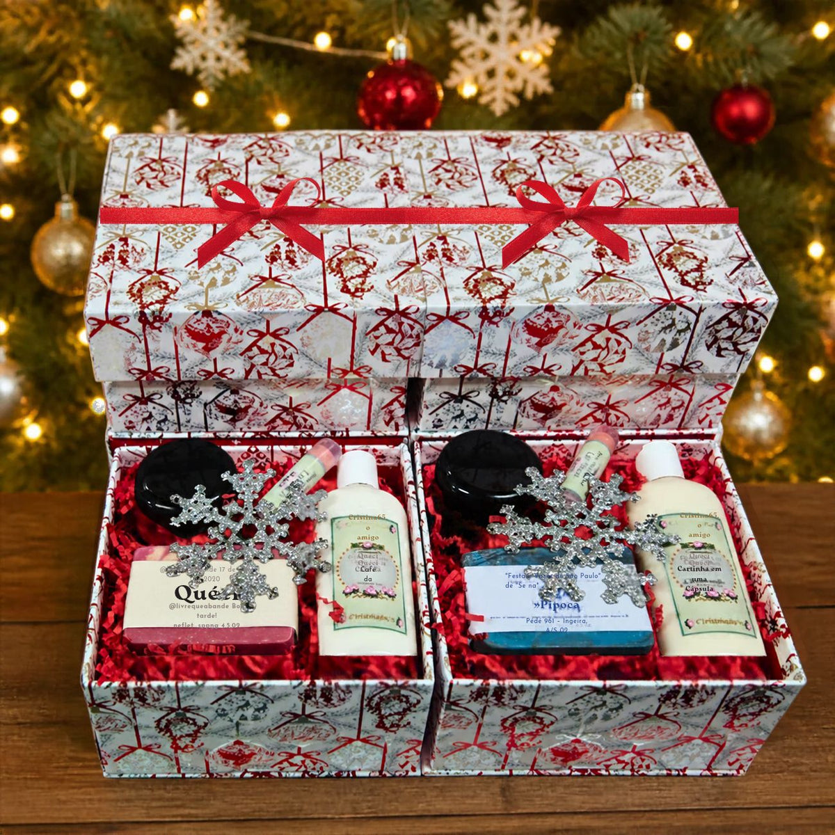 Two open customizable holiday gift boxes displaying the Queen and blue artisan soap gift sets with matching lotions and body jars, sitting below a stacked matching closed box with a red ribbon against a glowing, festive Christmas tree bokeh background.