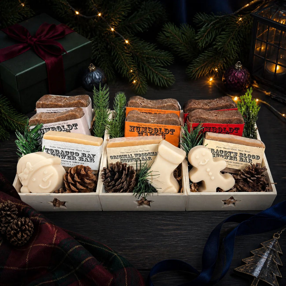 Three rustic wooden gift crates with star cutouts, each packed with two textured Humboldt Hands hand soaps, a smooth goat milk shower bar (in Tobacco Bay, Original Woodsman, or Dragon&