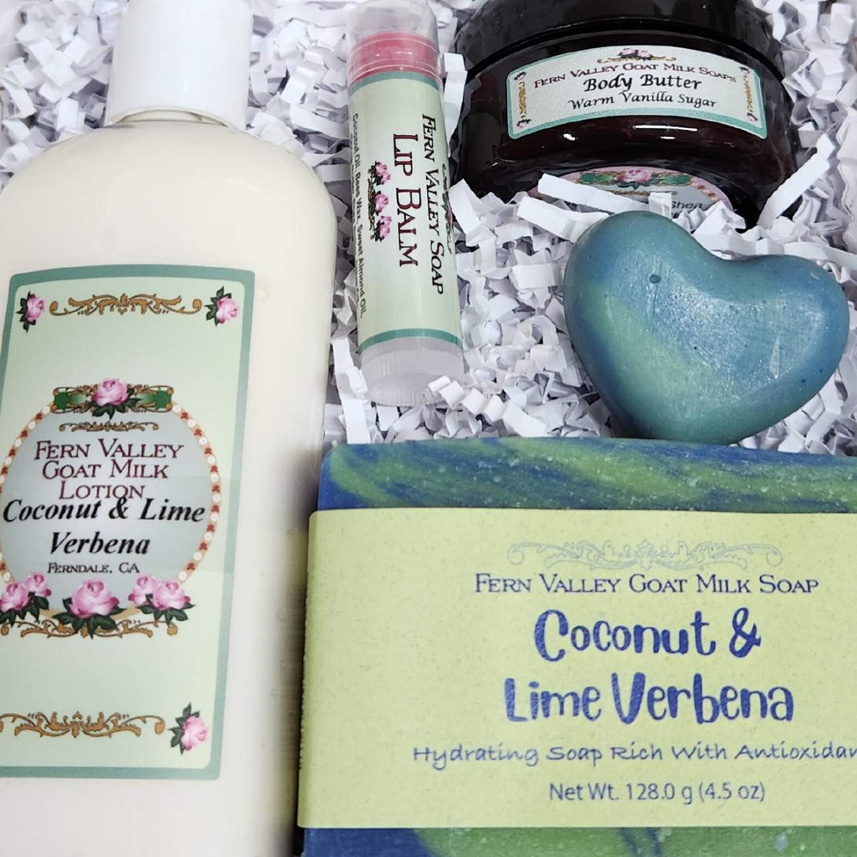 Coconut Lime Verbena goat milk soap, matching lotion, a heart novelty soap, vanilla body butter, and a lip balm on white crinkle paper.