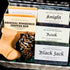 A plaid holiday gift box filled with Fern Valley Goat Milk Soaps for men, including Original Woodsman, Rook, and Black Jack bars, next to a boot-shaped soap and pinecones.