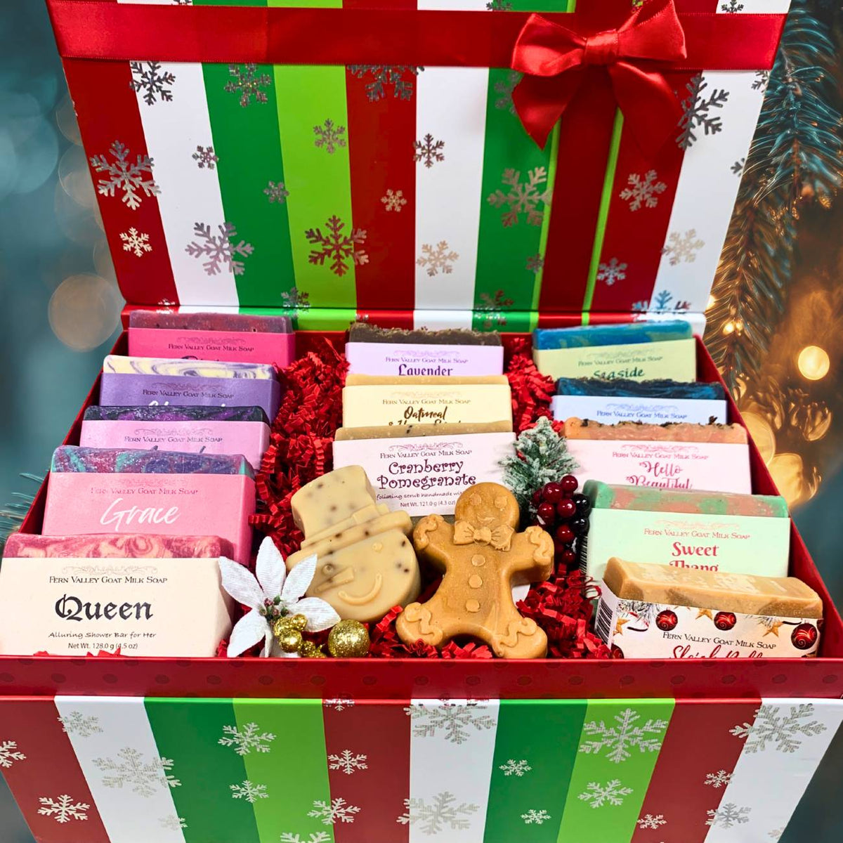 Open festive red and green snowflake Christmas box revealing 13 handcrafted Fern Valley goat milk soaps, a gingerbread man soap, and a snowman soap nestled in red crinkle paper.